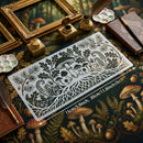 A rectangular white stencil or template sheet with a black forest and mushroom illustration, laid on a dark patterned surface. The sheet includes overlaid size arrows and text reading 15cm/5.