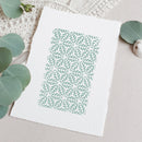 A square white art print with a mint green geometric leaf pattern, styled on a neutral beige surface with eucalyptus leaves and a textured cream fabric background.