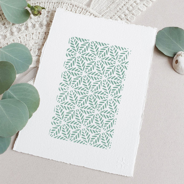 A square white art print with a mint green geometric leaf pattern, styled on a neutral beige surface with eucalyptus leaves and a textured cream fabric background.
