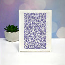 A framed art print featuring a lavender purple background with dense white abstract cursive line patterns, displayed on a white surface next to a small potted succulent against a pastel purple and blue bokeh background.