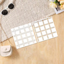 Two square white fabric or paper squares with a beige plaid grid pattern are laid on a light wood surface next to a cream woven textile, sunglasses, a small handbag, and flowers.