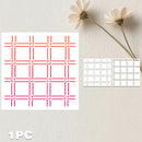 A square stencil or template sheet with a red-orange and pink plaid grid pattern, shown alongside two smaller white stencil sheets with gray grid lines on a light textured background with dried flowers.