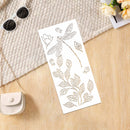 A white rectangular sheet with elegant gold-toned botanical line drawings, including a dragonfly, flowers, and leaves, styled on a light wood surface with a woven textile, sunglasses, a small purse, and flowers.