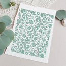 A square art print with a mint green damask pattern on a white background, styled on a textured beige surface with eucalyptus leaves and a small shell.