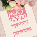 A white stencil sheet featuring pink dripping paint and hexagonal pattern designs, styled with pink roses and green leaves on a light beige fabric background.