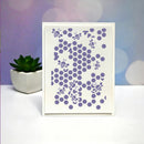 A white rectangular card or print featuring a lavender-purple honeycomb pattern with scattered bee silhouettes, standing on a white surface against a soft pastel purple and blue blurred background. A small potted succulent sits to the left.