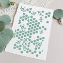 A square white art print with a mint green honeycomb and bee pattern, styled flat-lay on a neutral beige surface with eucalyptus leaves and a crochet blanket.