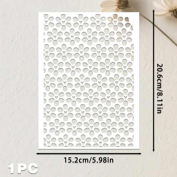 A white rectangular stencil or template with a repeating floral cutout pattern, shown on a light textured background with dimension arrows indicating 15.2 cm by 20.
