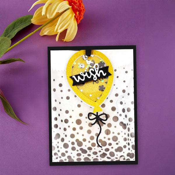 A handmade greeting card featuring a yellow balloon design with the word 'wish' on a black banner, set against a purple background with a yellow flower prop.