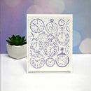 A vertical white greeting card featuring a collage of purple pocket watch illustrations, standing on a white surface with a small potted succulent and a purple bokeh background.