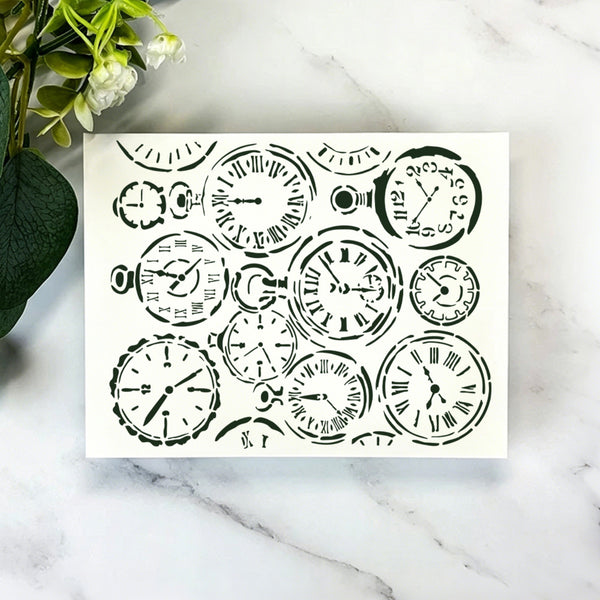 A square white art print or card featuring a collage of black vintage pocket watch illustrations, displayed on a white marble surface with green leaves and white flowers in the corner.