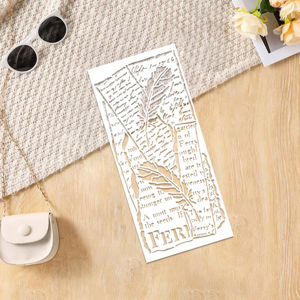 A white rectangular laser-cut paper bookmark with a leaf and script design, styled on a light wood surface with a textured cream fabric, sunglasses, a small purse, and flowers.