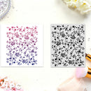 Two square floral stencil sheets displayed on a white surface. The left sheet has a pink-to-purple-to-blue floral vine pattern on white, and the right sheet has a black floral vine pattern on gray.