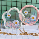 Two handmade clear plastic shoulder bags with crocheted handles, one in white and one in pink, filled with pastel beads and decorated with white daisy patches. The bags have gold chain straps and are displayed on a white surface with a green tiled background.