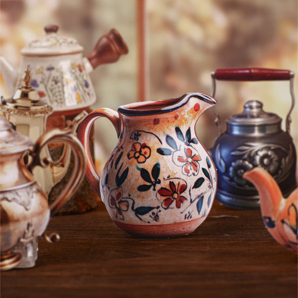 Decorative ceramic pitcher with floral patterns on a wooden surface with other ceramic items.