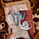Decorative teapot and pitcher pins on a textured surface with vintage paper and flowers.