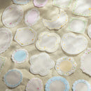A collection of small, pastel-colored fabric patches with scalloped edges and embroidered floral details, arranged on a textured beige fabric background.