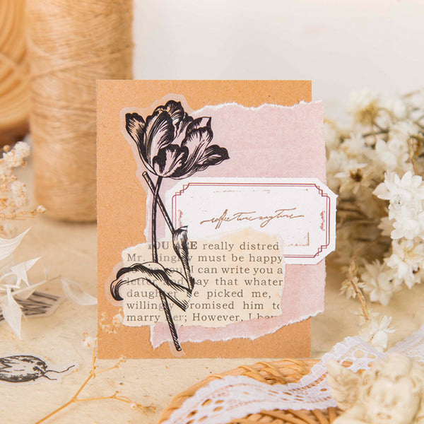 A handmade vintage-style greeting card with torn paper elements, featuring a black tulip illustration and a decorative label, styled on a neutral background with dried flowers and twine.