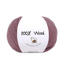 A ball of dusty mauve purple 100% wool yarn with a white paper label that reads '100% Wool' and features a small sheep illustration, set against a plain white background.