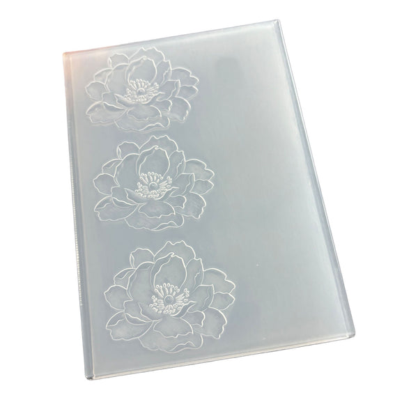 A rectangular translucent plastic mold or stamp with three embossed white floral designs, shown on a plain white background.