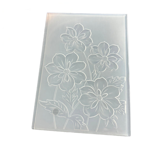 A rectangular translucent plastic mold or stamp featuring an embossed floral pattern of four large flowers and leaves, shown on a plain white background.
