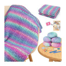 A multicolor crochet blanket with pink, blue, and purple stripes draped over a wooden chair, alongside folded blankets, yarn balls, knitting needles, and a pattern booklet on a white background.