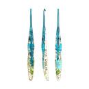 Three glass crochet hooks with blue handles and embedded gold foil and green botanical details, arranged vertically on a plain white background.