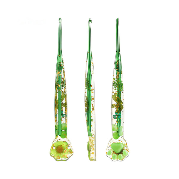 Three green glass crochet hooks with embedded dried flowers and gold foil, shown from front, side, and back views on a white background.