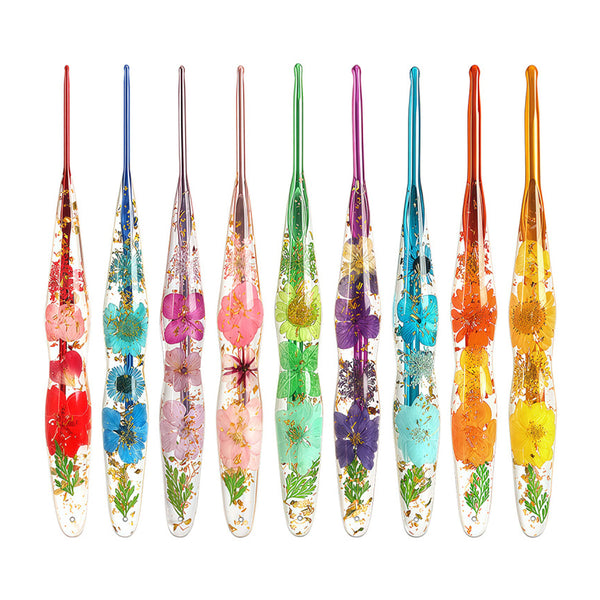 Eight colorful glass nail art tools with embedded pressed flowers and gold foil, arranged in a row on a white background.