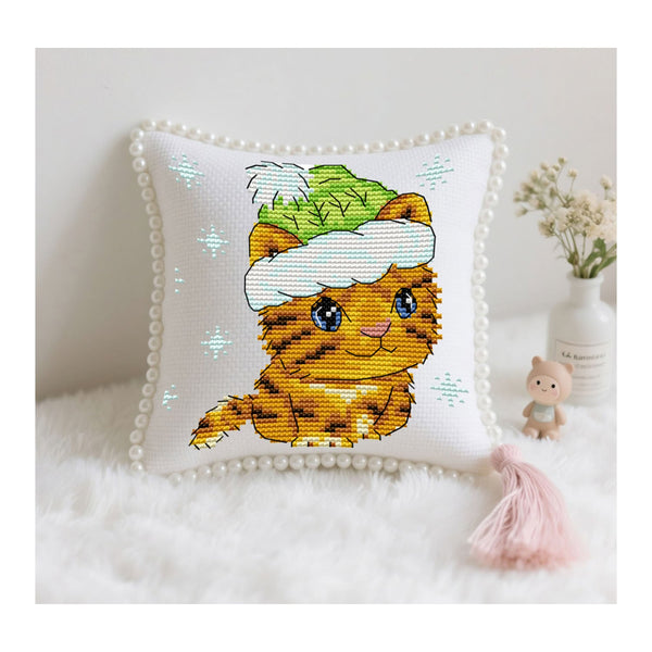 Cross-stitched pillow with a cat design wearing a hat on a white surface.