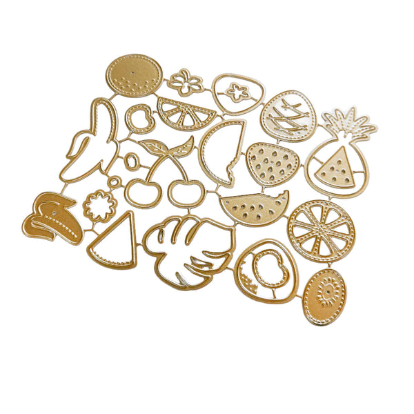 A set of gold-colored metal fruit and vegetable cutters or stamps arranged on a plain white background, including designs like a pineapple, strawberry, cherry, watermelon slice, citrus, and leaf motifs.
