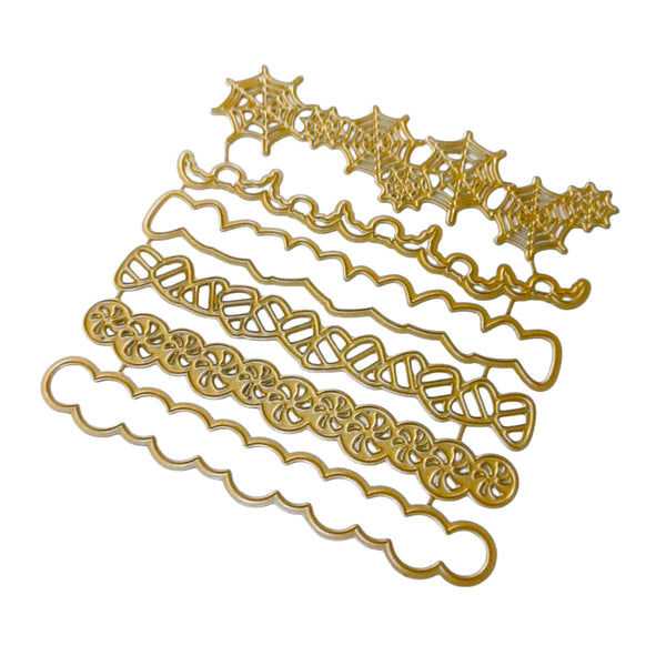 A set of gold metal embossing or cutting dies arranged diagonally on a plain white background, featuring various Halloween-themed designs including spiderwebs, bats, and skulls.