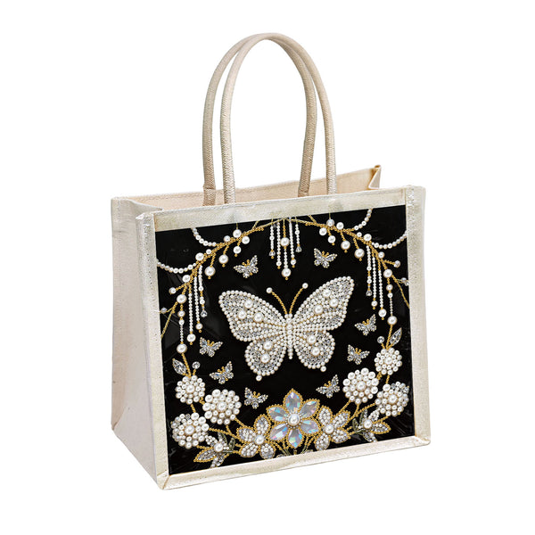 A structured tote bag with a black front panel featuring an intricate rhinestone and bead butterfly and floral design, finished with cream-colored handles and trim.
