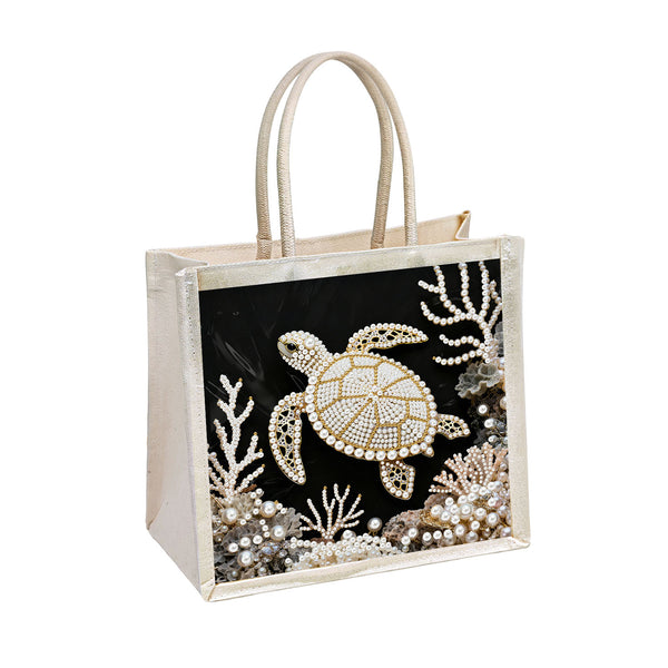 A square canvas tote bag with cream-colored handles and trim, featuring a black front panel decorated with a sea turtle and coral reef designs made from white pearls and beads.