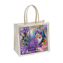 A square canvas tote bag with cream-colored handles and trim, featuring a colorful printed illustration of a purple cat in a floral forest scene on the front.