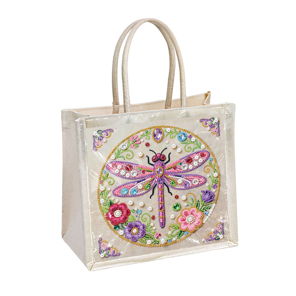 A clear plastic tote bag with beige handles, featuring a colorful embroidered dragonfly and floral design on the front, set against a plain white background.