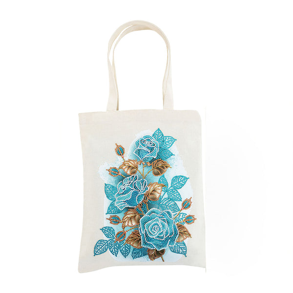 An off-white canvas tote bag featuring a detailed floral design of blue and teal roses with gold and brown leaves, set against a plain white background.