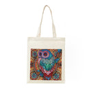 An off-white canvas tote bag with long handles, featuring a colorful, highly detailed owl illustration printed on the front. The owl is decorated with intricate patterns in shades of teal, blue, pink, and gold against a dark background.
