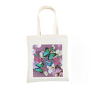 An off-white canvas tote bag with a square printed graphic on the front featuring green, pink, and blue butterflies on a purple background, set against a plain white studio backdrop.