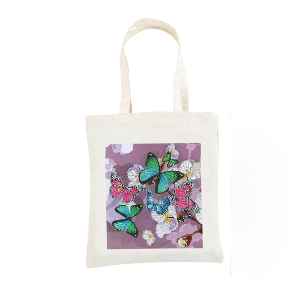 An off-white canvas tote bag with a square printed graphic on the front featuring green, pink, and blue butterflies on a purple background, set against a plain white studio backdrop.