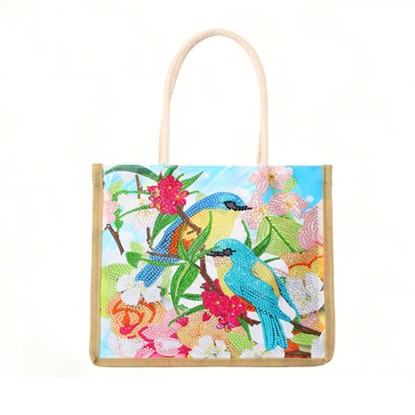A square canvas tote bag with a colorful beaded bird and floral design on the front, featuring natural beige handles and trim, set against a plain white background.