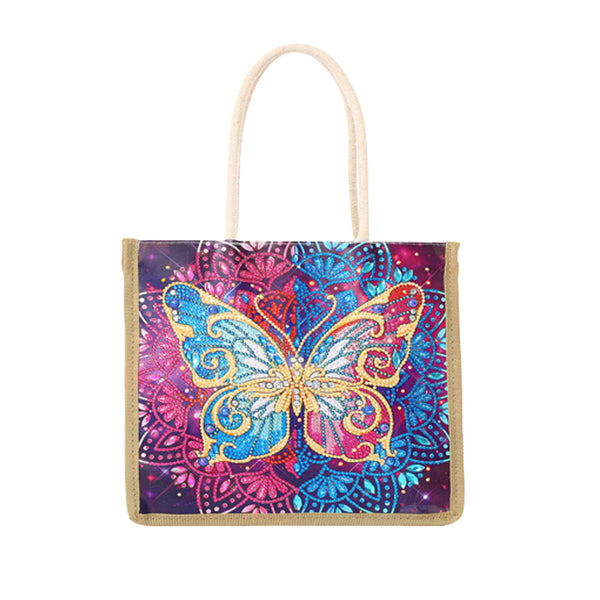 A square canvas tote bag with a colorful printed design featuring a glittery blue and gold butterfly over a purple and pink mandala pattern, finished with natural beige rope handles and beige trim.