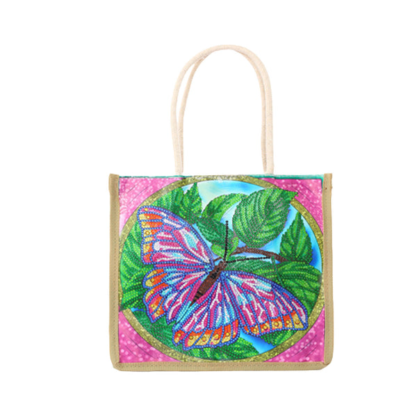 A square canvas tote bag with cream-colored rope handles, featuring a colorful beaded butterfly and leaf design on a pink glittery background.