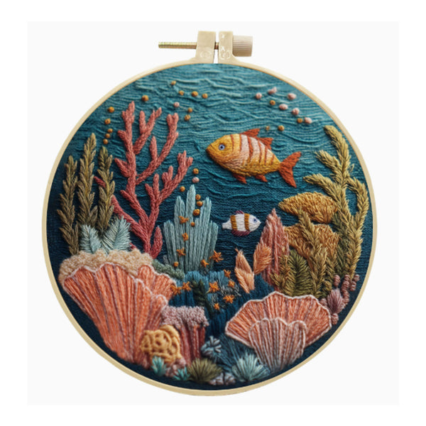 A circular embroidery hoop containing a colorful embroidered underwater scene with coral, sea plants, and two fish on a light gray background.