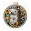 A circular embroidery hoop containing a finished embroidered hedgehog surrounded by yellow, orange, and white flowers on a light gray fabric background.