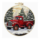 A circular embroidery piece in a wooden hoop, depicting a vintage red pickup truck driving through a snowy winter forest with pine trees under a pale sky.