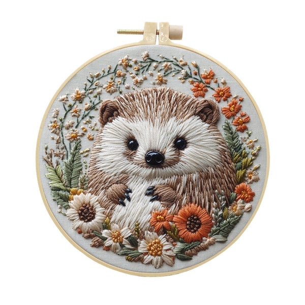 A circular embroidery hoop holding a detailed stitched hedgehog surrounded by small flowers and leaves on a white background.