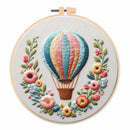 Embroidered circular wall art in a wooden hoop, featuring a colorful hot air balloon surrounded by delicate flowers on a white background.