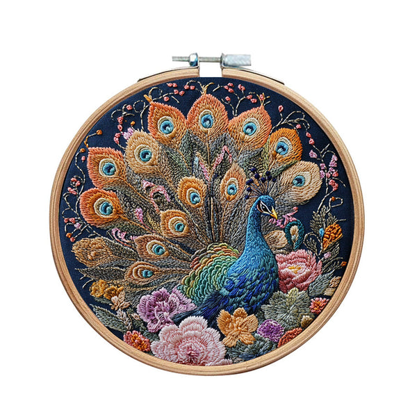 A circular wooden embroidery hoop containing a detailed peacock and floral design stitched in vibrant threads on a dark navy background, shown against a plain white background.
