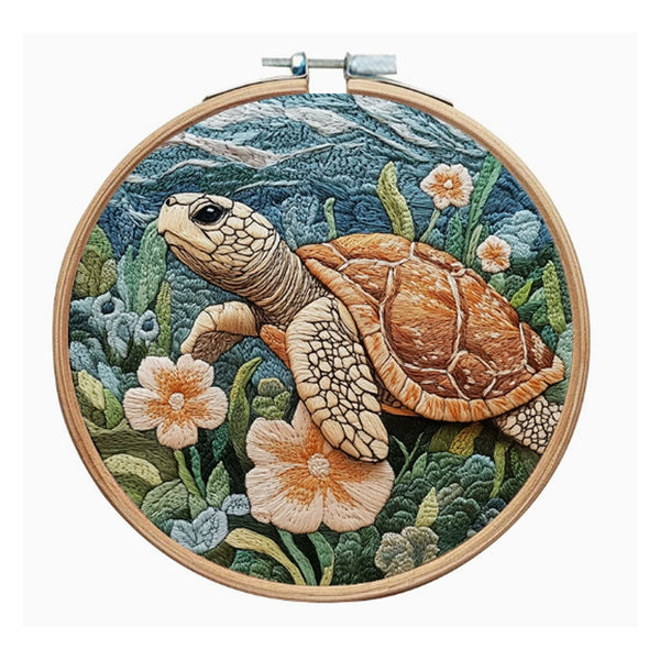 A circular wooden embroidery hoop holding a detailed needlepoint or embroidered sea turtle scene with blue-green water, green plants, and peach flowers, shown against a plain white background.